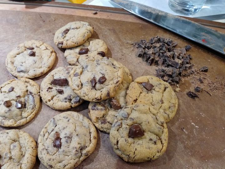 Freshly baked chocolate chip cookies beside chopped chocolate on a board