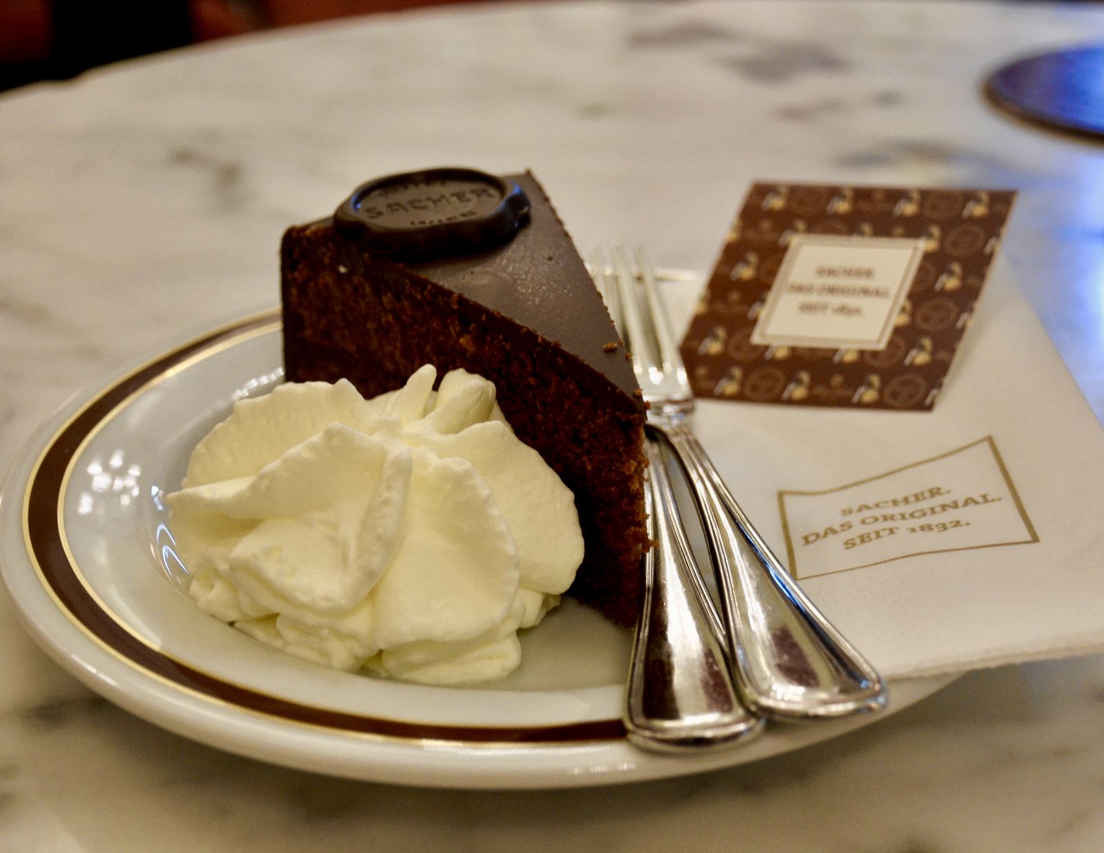A slice of Sachertorte with whipped cream on a plate in Vienna
