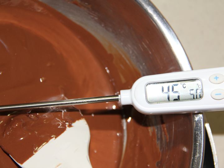 A thermometer in a bowl of melted chocolate during tempering